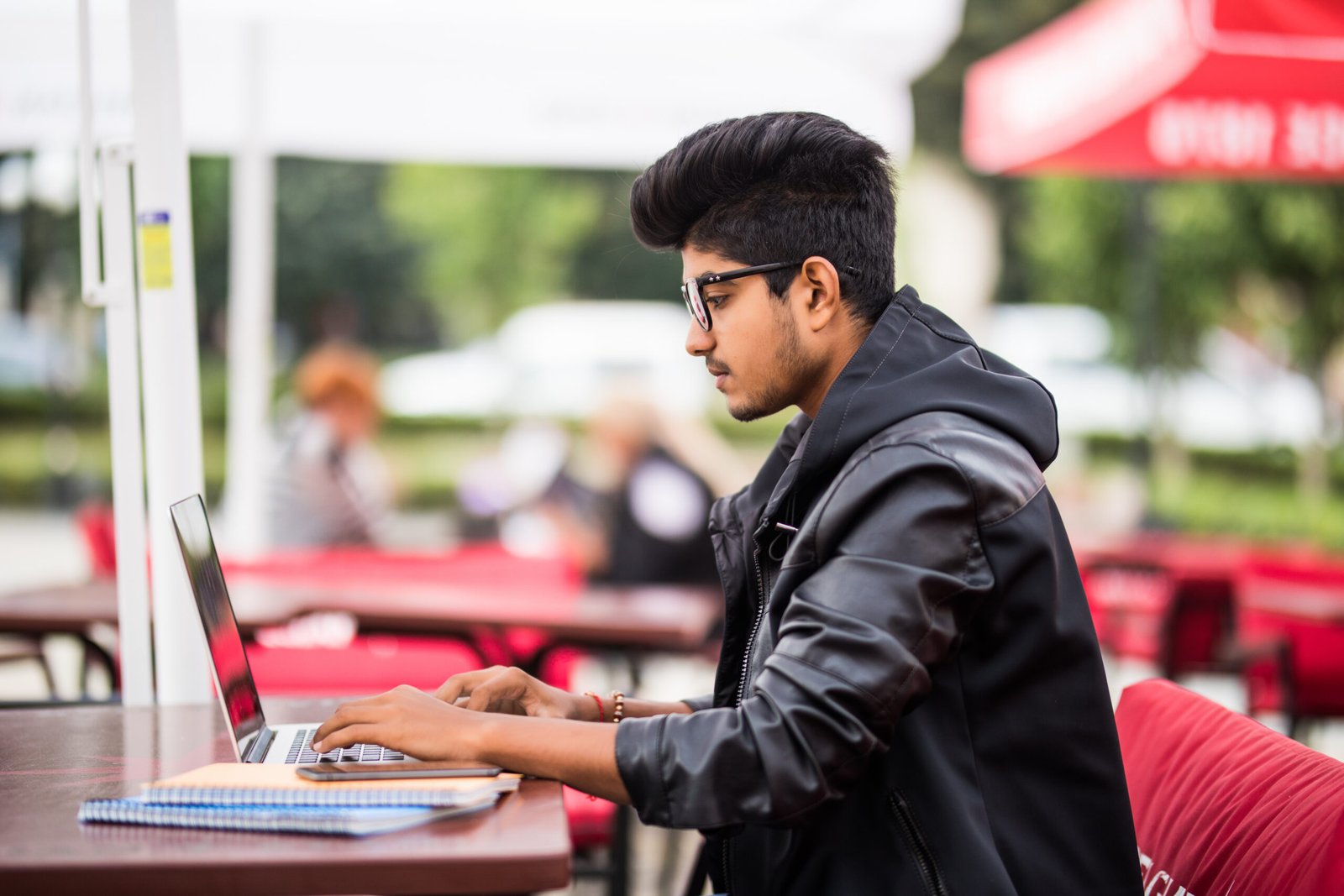 Indian man using laptop while drinking a cup coffee, outdoor street cafe